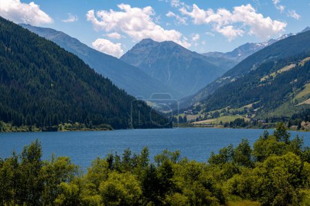 Artificial alpine reservoir lake Zoccolo Zoggler-Stausee and mountain range at Ultental, South Tyrol Italy on sunny summer day. 