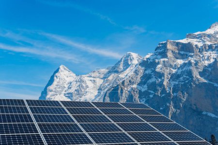 Contemporary photovoltaic cells installed on rooftop against snowy mountain range under blue sky on sunny day