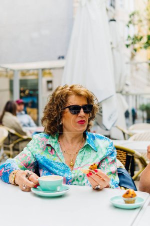 Photo for Vertical photo with copy space of a mature modern woman with sunglasses having breakfast on an outdoor cafeteria - Royalty Free Image