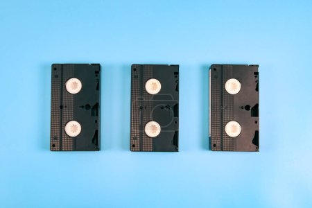 Foto de Three retro videotapes lie in the middle on a blue background, top view, close-up. Cinema concept. - Imagen libre de derechos