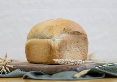 Foto de One small square wheat white bread on a wooden cutting board lies on a table in the kitchen against a blurred brick wall,close-up bottom view.Bread baking concept. - Imagen libre de derechos