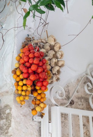 Foto de Beautiful view of bunches of tomato, lemons and garlic hanging on the wall of a drying house in the city of Ostuni, Italy, close-up side view. The concept of ancient architecture. - Imagen libre de derechos