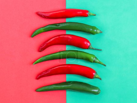 Foto de Six hot green and red chili peppers lie vertically in a row on a red-green background, flat lay close-up. The concept of Cinco de Mayo, minimalism, blanks. - Imagen libre de derechos