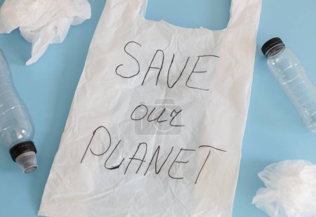 Foto de Una bolsa de plástico blanco con la inscripción en marcador negro - salvar nuestro planeta y botellas de plástico se encuentran en diagonal sobre un fondo azul, vista lateral de primer plano.Concepto del día de la Tierra, reciclaje. - Imagen libre de derechos