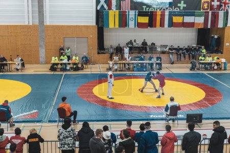 Téléchargez les photos : Dalfsen, Pays-Bas - 11 mars 2023 - Photo en gros plan de deux jeunes lutteurs de sambo qui se battent lors d'un tournoi international de sambo et d'un juge qui les regarde. - en image libre de droit