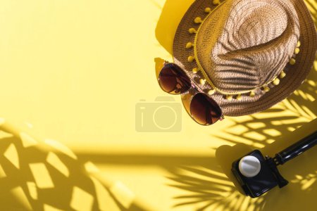 Camera, sunglasses and straw hat on the right on a yellow background with palm branches shadow, sun glare and copy space on the left, flat lay close-up. Summer concept, blogger. mug #648402420