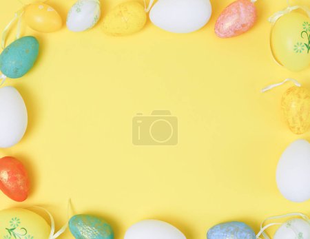 Foto de Decorative Easter eggs are arranged in a square frame on a yellow background with copy space in the center, flat lay close-up. Happy Easter concept, banner, blanks. - Imagen libre de derechos