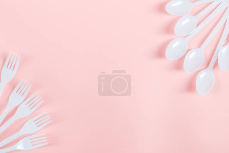 Foto de Tenedores de plástico blanco y cucharas se encuentran en los lados sobre un fondo rosa claro con espacio de copia para el texto en el centro, plano de primer plano. El concepto de ecología, basura plástica y vajilla plástica desechable. - Imagen libre de derechos