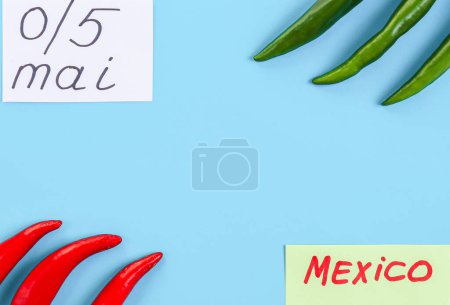 Foto de Los chiles picantes verdes y rojos se encuentran en los lados con notas: 5 de mayo y mexico sobre un fondo azul con espacio para copiar, plano de primer plano. El concepto de Cinco de Mayo, minimalismo, espacios en blanco. - Imagen libre de derechos