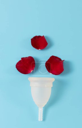 Photo for A silicone menstrual cup and three red rose petals lie in the center on a blue background, flat lay close up. Woman health concept. - Royalty Free Image