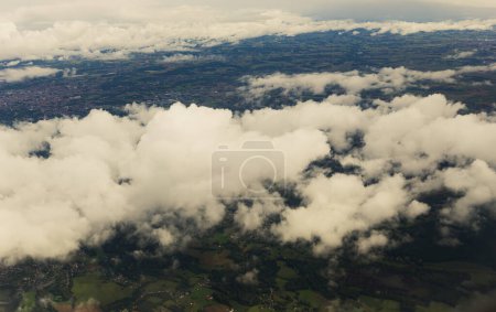 Foto de Hermosa vista aérea de nubes de cúmulos blancos y la tierra con campos, árboles y asentamientos, vista de cerca desde la parte superior desde una ventana de avión. - Imagen libre de derechos