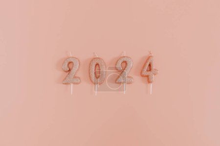 Photo for Shiny candles with the number 2024 lie in a row in the center on a pink background, flat lay close-up. - Royalty Free Image