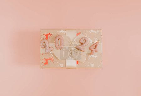 Photo for Shiny candles with the number 2024 on a gift box tied with a bow lie in the center on a pink background, flat lay close-up. - Royalty Free Image