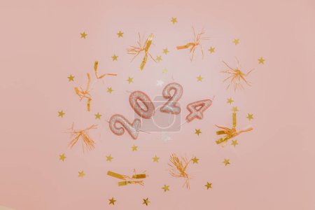 Photo for Shiny candles number 2024 with gold tinsel and confetti lie in a round frame in the center on a pink background, flat lay close-up. - Royalty Free Image