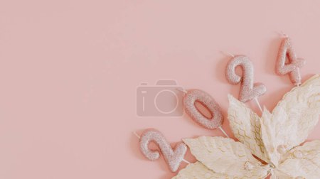 Photo for Shiny candles number 2024 with gold foliage lie on the right on a pink background with copy space on the left, flat lay closeup. - Royalty Free Image