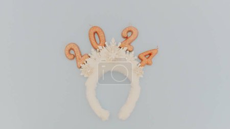 Photo for Cute baby headband tiara with white snowflakes and light brown sparkly candles number 2024 lie in the center on a pastel blue background with copy space on the sides, flat lay close-up. - Royalty Free Image