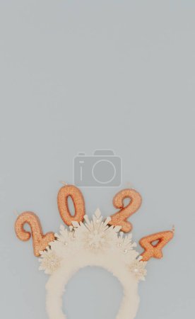 Photo for Cute baby headband tiara with white snowflakes and light brown sparkly candles number 2024 lie in the bottom on a pastel blue background with copy space on top, flat lay close-up. - Royalty Free Image