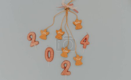 Photo for One holiday decoration with wooden angels, motivational words hanging on a blown string and light brown glitter candles number 2024 lies in the center on a pastel blue background, flat lay close-up. - Royalty Free Image