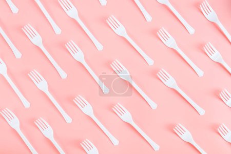 Foto de Una gran cantidad de horquillas de plástico blanco se encuentran en diagonal sobre un fondo rosa claro, plano de primer plano. El concepto de ecología, basura plástica y vajilla plástica desechable. - Imagen libre de derechos
