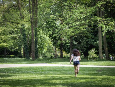 One beautiful Caucasian brunette girl from the back is running on a summer day in a public park, close-up side view.