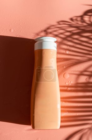 One bottle of liquid soap lies in the center in a plate on a pastel peach background with shadows from a palm branch and drops of water, flat lay close-up.
