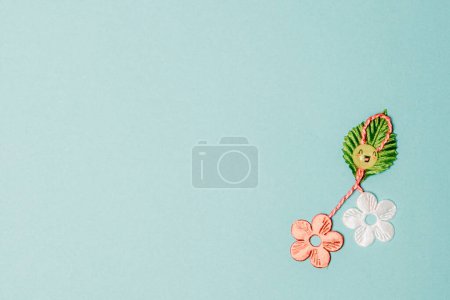 Photo for One beautiful homemade martisor made from flowers, a petal and a cheerful smiley face lies in the lower right corner on a light blue background with copy space on the left, flat lay close-up. - Royalty Free Image