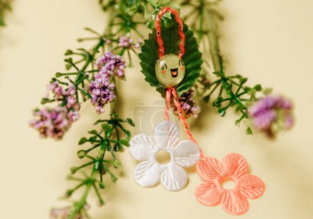Photo for One beautiful homemade martisor of two flowers, a petal and a cheerful smiley face with a bouquet of spring flowers lies on a pastel yellow background, close-up side view. - Royalty Free Image