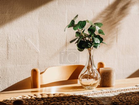 Téléchargez les photos : Un vase transparent en verre avec des branches d'eucalyptus et un support de bougie sur une table de cuisine en bois contre le mur un soir d'été, vue latérale rapprochée. - en image libre de droit