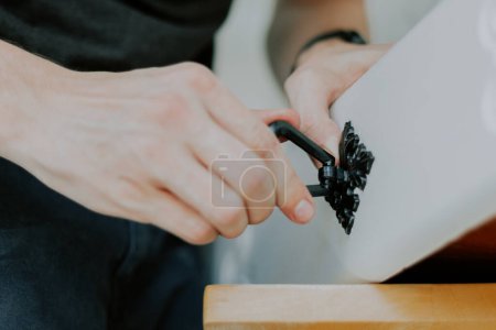 Téléchargez les photos : Les mains d'un jeune homme caucasien méconnaissable enlève une poignée noire sculptée antique sur un tiroir blanc, vue latérale rapprochée. - en image libre de droit