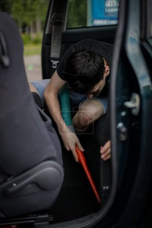 Un guapo joven caucásico morena chico sostiene un tubo con una boquilla en las manos y aspira el asiento en el coche, vista lateral de cerca.