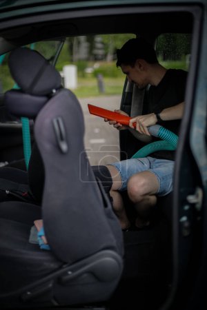 Un beau jeune mec brune caucasien tient un tube avec une buse dans les mains et aspire le siège dans la voiture, vue de côté gros plan.