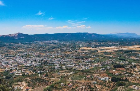 Belle vue panoramique d'un village avec végétation et routes situé sur une plaine près des montagnes avec un ciel bleu en Grèce sur l'île de Rhodes par une journée ensoleillée d'été, vue latérale rapprochée.