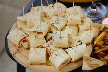 Appetizing appetizers for an aperitif of lavash with red smoked fish on wooden round dishes with toothpicks on a table in the backyard of a house on a sunny spring day, side view close-up.