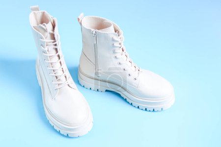 Bottes demi-saison blanches en éco-cuir avec semelle rugueuse et laçage sur fond bleu, vue latérale rapprochée. Le concept de chaussures pour femmes à la mode.