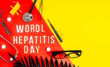 One stethoscope, white pills, yellow-red ribbon, glasses, surgical instruments, palm leaf and light wooden letters with the lined phrase world hepatitis day lie on the left on a red-yellow bright