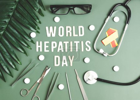 A stethoscope, a red yellow ribbon, surgical instruments, pills, glasses and light wooden letters with the lined phrase World Hepatitis Day lie in the center on a mint green background with
