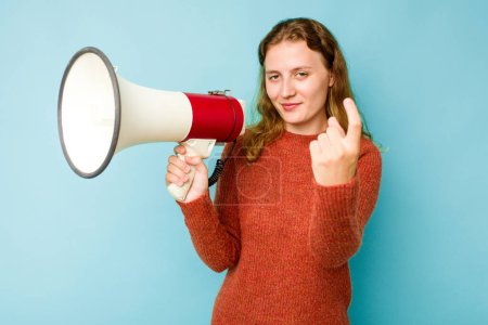 Téléchargez les photos : Jeune femme caucasienne tenant mégaphone isolé sur fond bleu pointant du doigt vers vous comme si invitant se rapprocher. - en image libre de droit