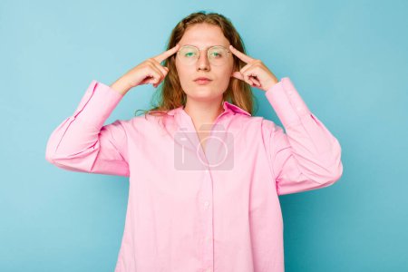 Photo for Young caucasian woman isolated on blue background focused on a task, keeping forefingers pointing head. - Royalty Free Image