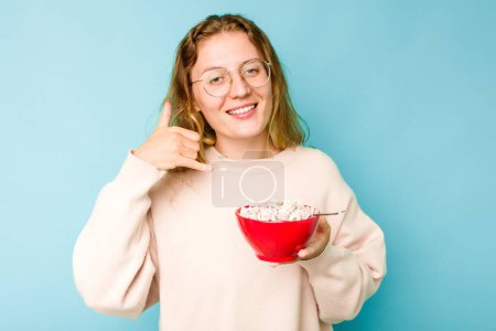 Photo for Young caucasian woman holding a bowl of cereals isolated on blue background showing a mobile phone call gesture with fingers. - Royalty Free Image
