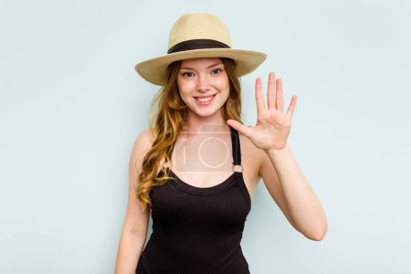 Foto de Joven mujer caucásica que va a la playa aislada sobre fondo azul sonriente alegre mostrando el número cinco con los dedos. - Imagen libre de derechos