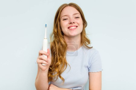 Téléchargez les photos : Jeune femme caucasienne tenant une brosse à dents électrique isolée sur fond bleu riant et s'amusant. - en image libre de droit