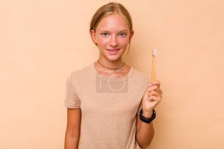 Téléchargez les photos : Caucasien adolescent fille brossage dents isolé sur fond beige heureux, souriant et joyeux. - en image libre de droit