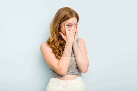 Photo for Young caucasian woman isolated on blue background blink through fingers frightened and nervous. - Royalty Free Image