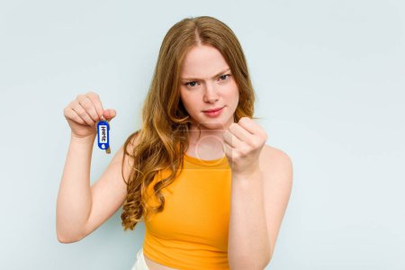Foto de Young caucasian woman holding home keys isolated on blue background showing fist to camera, aggressive facial expression. - Imagen libre de derechos