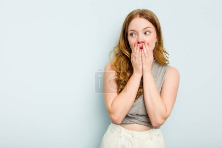 Téléchargez les photos : Jeune femme caucasienne isolée sur fond bleu réfléchi regardant vers un espace de copie couvrant la bouche avec la main. - en image libre de droit