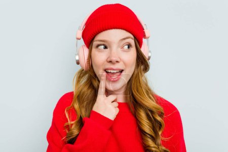 Téléchargez les photos : Jeune femme caucasienne portant des écouteurs isolés sur fond bleu - en image libre de droit