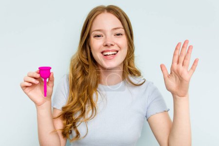 Téléchargez les photos : Jeune femme caucasienne tenant la coupe menstruelle isolée sur fond bleu recevant une agréable surprise, excitée et levant les mains. - en image libre de droit