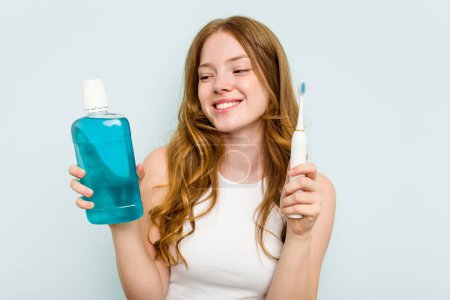 Téléchargez les photos : Jeune femme caucasienne tenant un rince-bouche et une brosse à dents isolés sur fond bleu - en image libre de droit