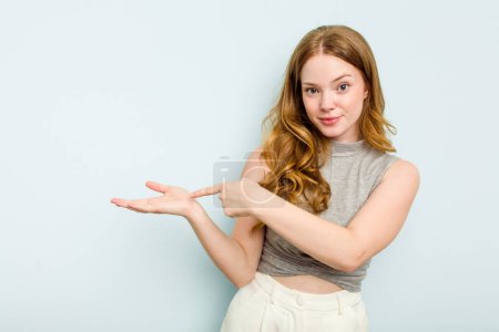 Photo for Young caucasian woman isolated on blue background excited holding a copy space on palm. - Royalty Free Image