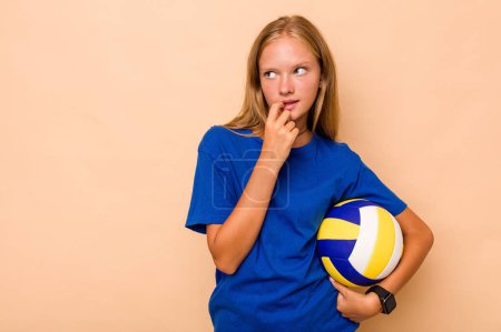 Téléchargez les photos : Petite fille caucasienne jouant au volley-ball isolé sur fond beige détendu penser à quelque chose en regardant un espace de copie. - en image libre de droit